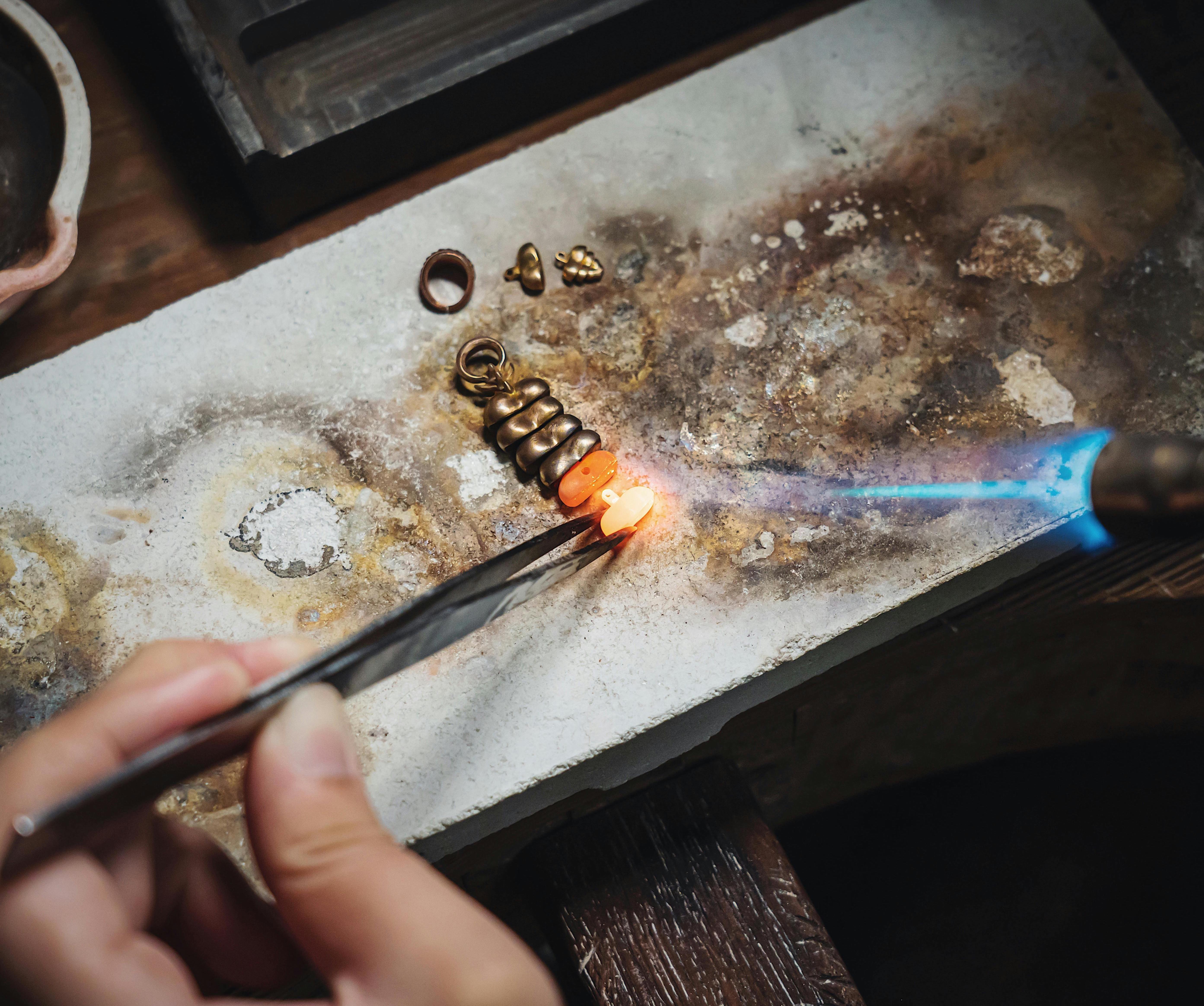 Jeweler heating gold components with a torch on a metal workbench