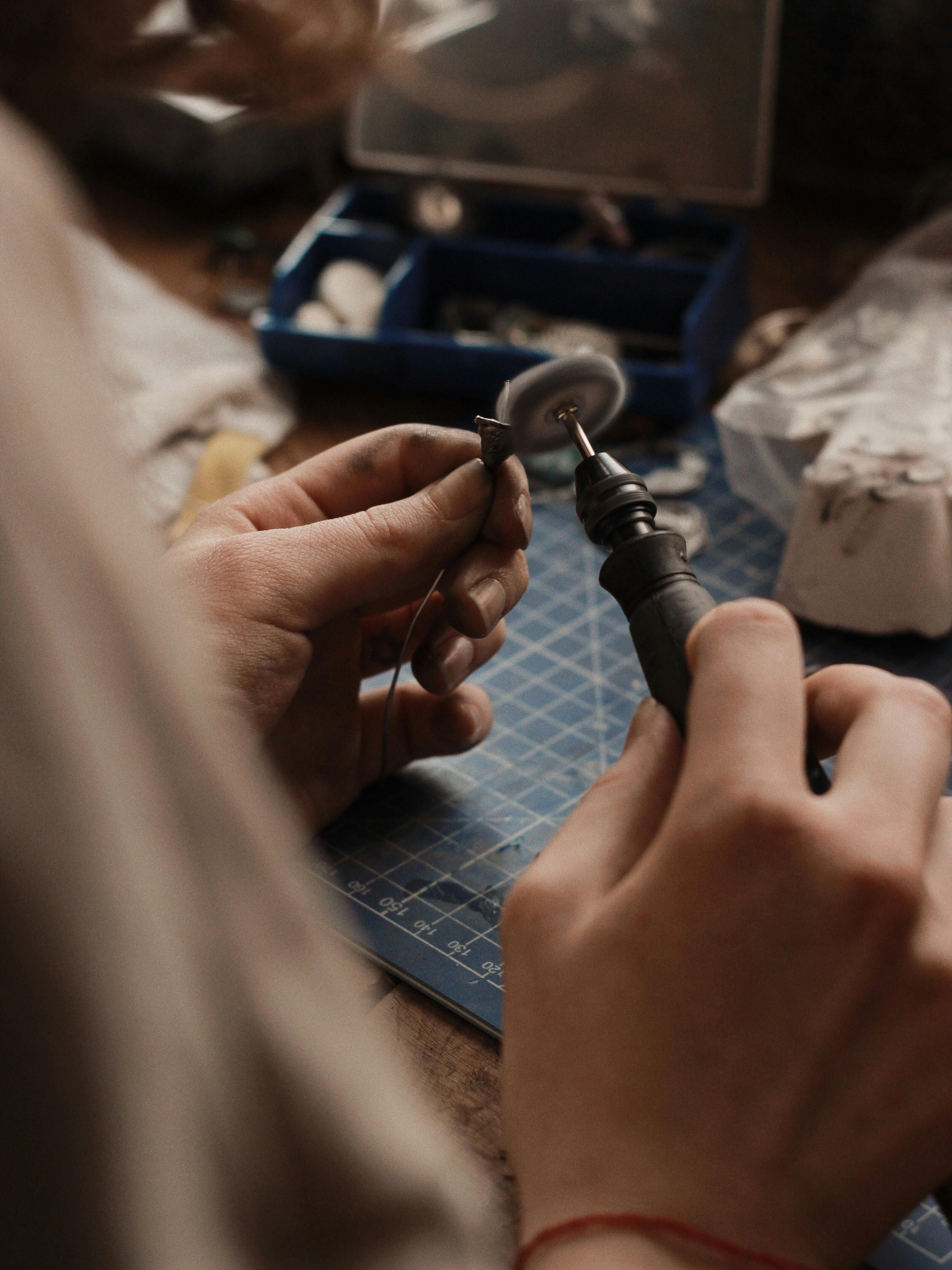 Jeweler polishing a small gold piece with a rotary tool at a workbench